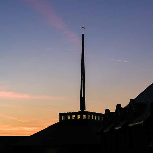 The spire of 博彩网址大全’s Jesuit Center seen at dusk with the setting sun behind it.